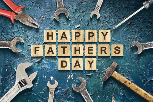 Happy Fathers Day inscription on wooden cubes with working tools on the Old Painted Iron. Greetings and gifts.