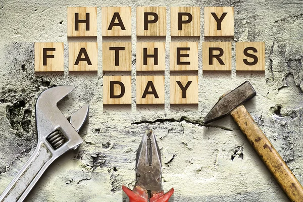 Happy Fathers Day inscription on wooden cubes with working tools on an old vintage concrete wall. Happy Father\'s Day Concept. Greetings and gifts. Holidays.