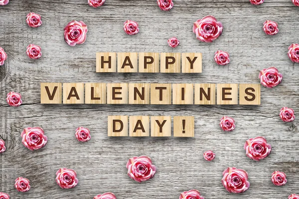 Happy Valentines Day, the inscription on the wooden cubes and buds of pink roses on a gray wooden background. Festive background. — Stock Photo, Image