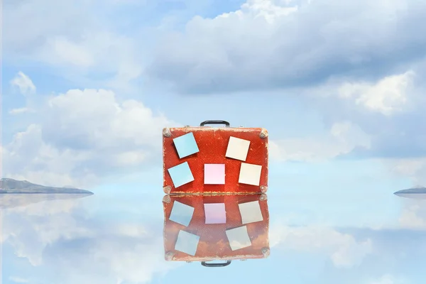 Old suitcase with empty stickers, with reflection, against blue sky with beautiful clouds. Copy space. Travel concept.