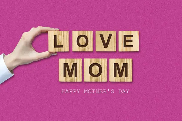 Glücklicher Muttertag Hintergrund. weibliche Hand und die Inschrift, love mom, auf Holzklötzen. rosa Hintergrund. Glückwunsch. — Stockfoto