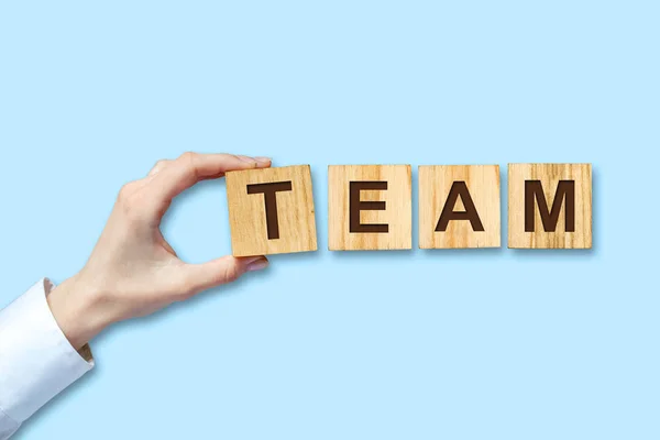 Concept, Team. Female hand in a white shirt holds in her hand a wooden block with the inscription, Team. Blue background. Isolated. Business background.