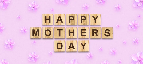 Glücklicher Muttertag, Wort auf Holzklötzen geschrieben. rosa Hintergrund mit Frühlingsblumen. Glückwunsch-Hintergrund. Urlaubskarte. — Stockfoto