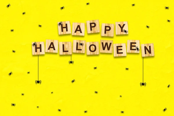 Happy Halloween, achtergrond. Veel kleine spinnen op een gele achtergrond. De inscriptie op houten blokken. Vakantie achtergrond. — Stockfoto