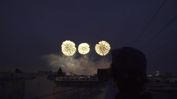 Jovem de pé no telhado do edifício alto olhando para fogos de artifício. Vista de trás — Vídeo de Stock