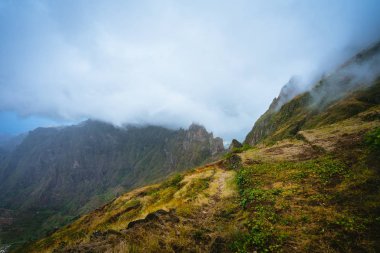 Yemyeşil çimen ile büyümüş ve ekili dağ tepe zinciri yanında trekking yolu bitkiler. Sisli bulutlar dağ kenar üzerinde hareket. XO-Xo Vadisi. Santo Antao Adası, Cape Verde Cabo Verde