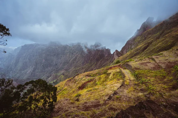 Trekking path along the mountain edge overgrown with verdant grass. Mountain peaks are covered by fog . Xo-Xo Valley. Santo Antao Island, Cape Verde Cabo Verde — Stock Photo, Image