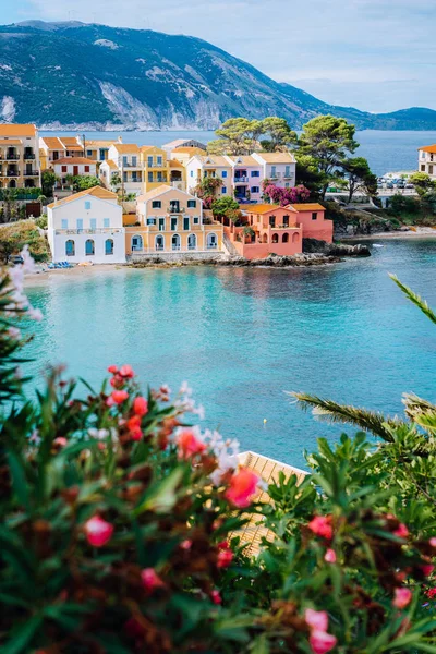 Цветные южные дома и синий залив Средиземного моря с красными цветами на переднем плане. Деревня Ассос в Кефалонии, Греция — стоковое фото