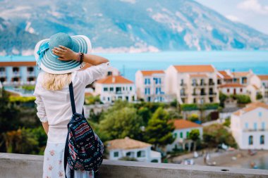 Manzaranın renkli sakin köyü Assos sabahı turist kadın. Mavi sunhat ve yaz seyahat etmek tatil Kefalonia, Yunanistan için zevk beyaz giysiler giyen genç şık kadın modeli