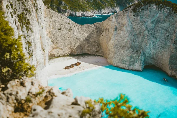 Famoso naufrágio na praia de Navagio com água azul-turquesa rodeada por enormes falésias brancas. Famosa localização histórica na ilha de Zakynthos, Grécia. Farme tiro entre as folhas — Fotografia de Stock