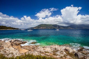 Kristal berraklığında şeffaf mavi turkuaz deniz mavisi Akdeniz deniz suyu Fiskardo şehirde. Çapa şaşırtıcı altında açık deniz yat beyaz bulutlar, Kefalonia, Ionian Islands, Yunanistan beyaz