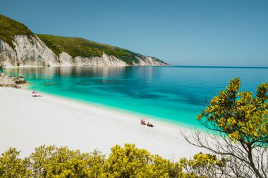 Amazing Fteri beach lagoon, Cephalonia Kefalonia, Greece. Tourists under umbrella relax near clear blue emerald turquise sea water. White rocks in background clipart