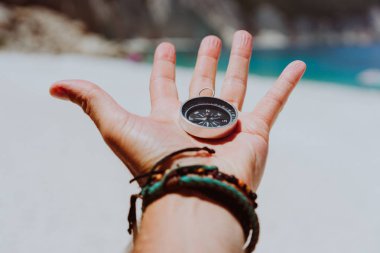 Avuç siyah metal pusula karşı beyaz kumlu plaj tutan gergin parmaklarını ile. Öyle ya da hedef kavramı bulmak. Bakış açısı pov