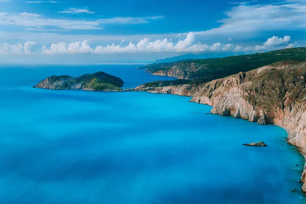 Vue sur la ville du village d'Assos et les ruines du château péninsulaire de Frourio. Belle baie bleue laiteuse avec une ligne de coûts en calcaire rocheux brun et des nuages blancs mouvants à l'horizon, île de Céphalonie, Grèce — Photo