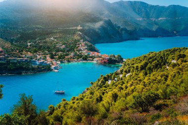 Assos köyü Kefalonia panoramik görünümü. Yunanistan. Kıyı şeridi boyunca çam ve selvi ağaçları çevrili güzel turkuaz renkli defne lagün su beyaz yalnız yat