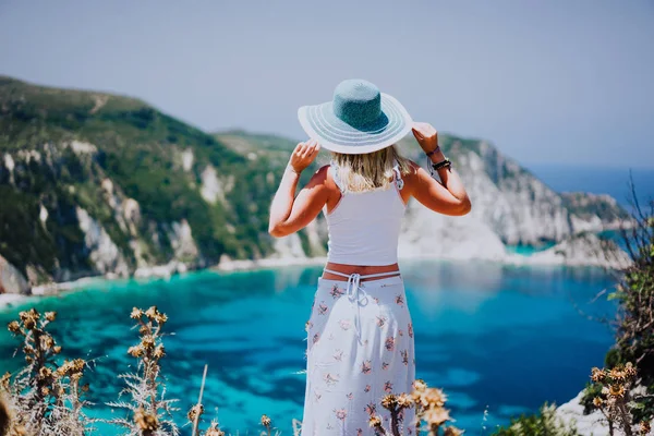 Jovem mulher na praia Petani Kefalonia, segurando chapéu de sol azul desfrutando de um panorama pitoresco da lagoa da baía azul esmeralda cercada por uma costa íngreme de penhascos. Grécia — Fotografia de Stock