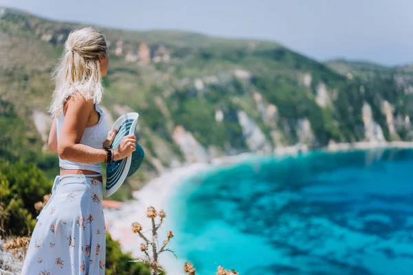 Mulher nova na frente da praia de Petani Kefalonia que admira o panorama pitoresco altamente excitado da baía emerald do mar Mediterranean e da ilha íngreme do litoral Greece — Fotografia de Stock