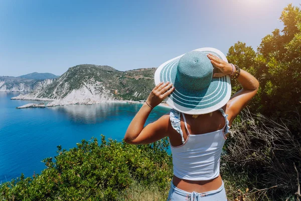 Praia Petani Kefalonia. Jovem mulher segurando chapéu de sol azul desfrutando de belo panorama da lagoa da baía azul cercada por penhasco íngreme litoral. Grécia — Fotografia de Stock