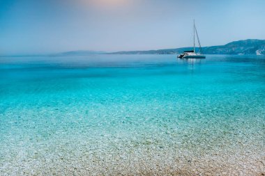 Pebble beach sakin saf temiz masmavi mavi su yüzeyi ile yakınındaki Katamaran yat tekne çapa, yelken