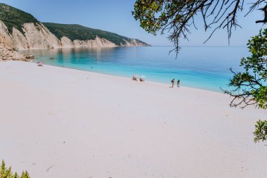 İnanılmaz Fteri beach lagün, Kefalonia, Yunanistan. Turistler şemsiye soğuk altında açık mavi zümrüt turkuaz deniz suyu sakin ol. Cliff rock kıyı şeridi arka planda