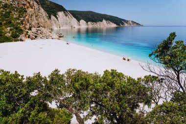Fteri beach, Kefalonia, Yunanistan. Yalnız turist şemsiye soğuk altında açık mavi zümrüt turkuaz deniz su lagoon sakin ol. Ağaç bitki örtüsü tarafından çerçeveli