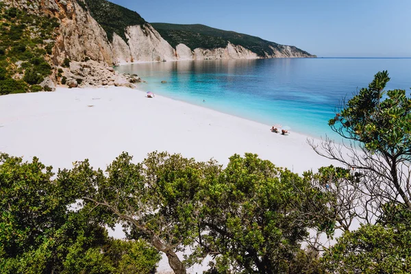 Plage de Fteri, Céphalonie, Grèce. Touristes solitaires sous le parapluie se détendre près clair bleu émeraude turquoise lagune d'eau de mer. Encadré par le feuillage des arbres — Photo