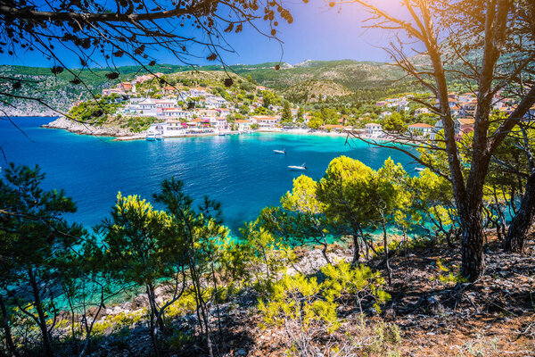 Pine tree grove branch frame view of Mediterranean sea bay in colorful Assos village. Kefalonia Greece