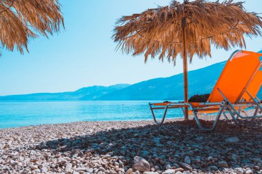 Sıcak gün batımı ışıkta saman şemsiyesi altında çakıl plajında şezlong Prange