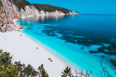Kireçtaşı kayalık sahil şeridi, Kefalonia, Yunanistan ile güneşli pastoral Fteri beach lagün. Turistler açık mavi zümrüt turkuaz deniz suyu altta koyu desenli yakınındaki şemsiyesi altında sakin ol