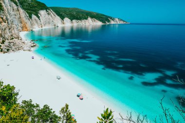 Güneşli Fteri beach lagün kayalık sahil şeridi, Kefalonia, Yunanistan ile. Turistler şemsiye soğuk altında açık mavi zümrüt turkuaz deniz suyu sakin ol.