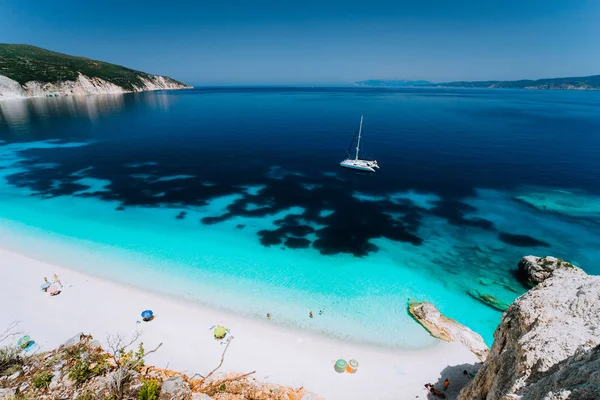 Lazurowymi wodami Fteri plaży Kefalonia Kefalonia, Grecja. Katamaran biały jacht w wodzie jasne błękitne morze. Turyści na piaszczystej plaży, w pobliżu laguny azure — Zdjęcie stockowe