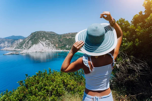 Praia Petani Kefalonia. Jovem mulher segurando chapéu de sol azul desfrutando de belo panorama da lagoa da baía azul cercada por penhasco íngreme litoral. Grécia — Fotografia de Stock