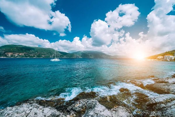 Crystal clear transparent blue turquoise teal Mediterranean sea water in Fiskardo town. White yacht in open sea at anchor under amazing white clouds and sun light, Kefalonia, Ionian islands, Greece — Stock Photo, Image