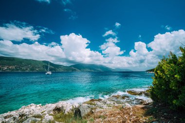 Kristal berraklığında şeffaf mavi turkuaz deniz mavisi Akdeniz deniz suyu Fiskardo şehirde. Çapa şaşırtıcı altında açık deniz yat beyaz bulutlar, Kefalonia, Ionian Islands, Yunanistan beyaz