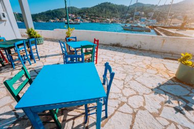 Renkli masa ve sandalyeler, güneşli teras. Denizin kenarında geleneksel kırsal Meyhanesi. Sıcak yaz gününde Yunan balıkçı köyü