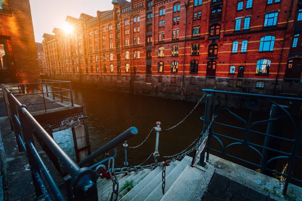 Um tijolo vermelho casas de vários andares de Speicherstadt Hamburgo. Famoso marco de velhos edifícios de tijolos vermelhos em luz dourada do pôr do sol. Vista panorâmica da noite com corrimão do canal em primeiro plano — Fotografia de Stock