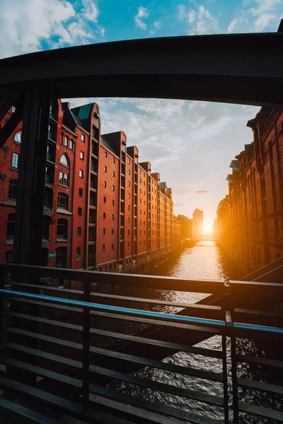 O armazém de tijolos vermelhos - distrito de Speicherstadt, em Hamburgo, Alemanha, emoldurado por vigas de arco de ponte de aço com perspectiva de canal preenchida por luz quente do pôr do sol — Fotografia de Stock