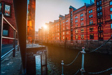 Kırmızı tuğla çok katlı Speicherstadt Hamburg ev sahipliği yapmaktadır. Altın günbatımı ışık eski tuğla binalar ünlü dönüm noktası. Doğal akşam görünümü ön planda kanal küpeşte ile