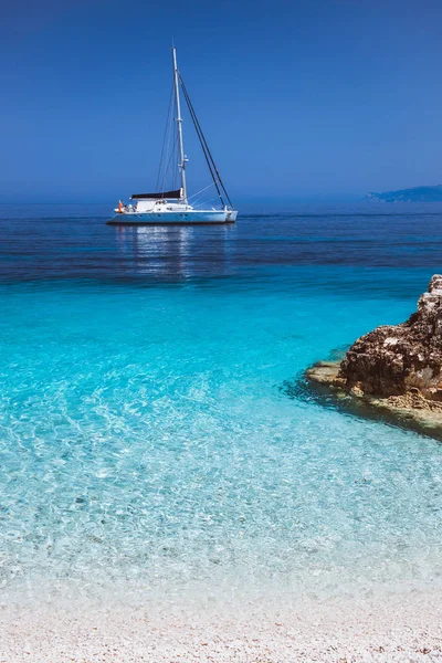 Beautiful calm azure blue lagoon with sailing catamaran yacht boat at anchor. Pure white pebble beach with rocks in the sea