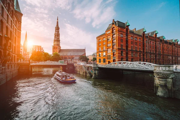 Touristic cruise boat on a channel with bridges in the old warehouse district Speicherstadt in Hamburg in golden hour sunset light, Germany — Stock Photo, Image