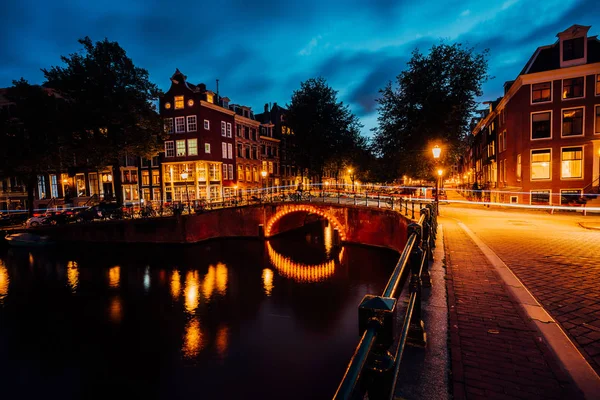 Geweldige overnachting in Amsterdam. Verlichte kanaal en brug met typisch Nederlandse huizen en fietsen, Holland, Nederland. Licht trails van de fietsen. Lange blootstelling — Stockfoto