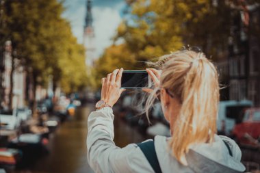 Kadın turist Amsterdam kanalda cep telefonunda bir resim çekmek. Sıcak altın öğleden sonra güneş ışığı. Avrupa'da seyahat