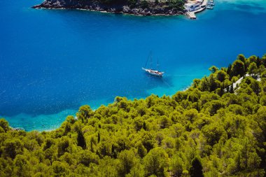 Üstten görünüm kıyı şeridi boyunca çam ve selvi ağaçları çevrili güzel turkuaz renkli defne lagün su beyaz yalnız yat. Assos village, Kefalonia Island, Yunanistan