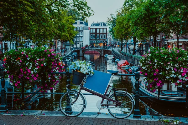 Levendige bloemen en fiets fiets op een brug van Amsterdam in de vroege avond. Schemering op het beroemde Unesco wereld erfgoed grachten van Amsterdam, Nederland — Stockfoto