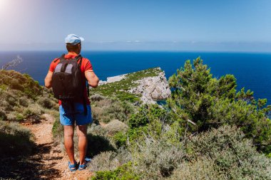 Turist adam güzel deniz manzarası önünde hiking. Sırt çantası ile kayalık iz yolda trekking fiyatı. Sağlıklı fitness yaşam tarzı açık havada kavramı Akdeniz Adası