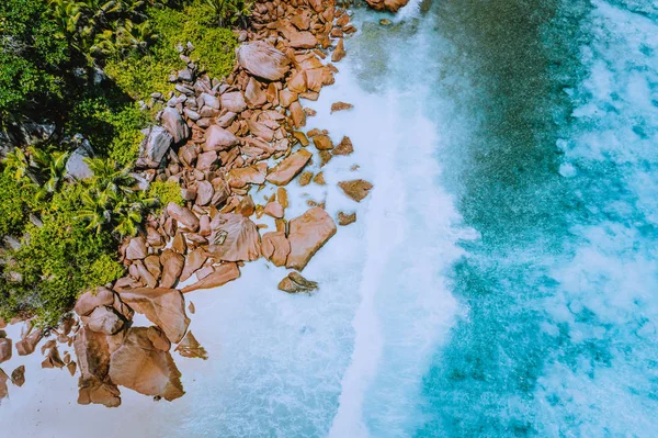 Seychelles La Digue Island. Aerial top view of ocean waves hitting huge bizarre granite rocks on the tropical beach anse cocos with turquoise azure water. Amazing rock cliff seascape in the coastline