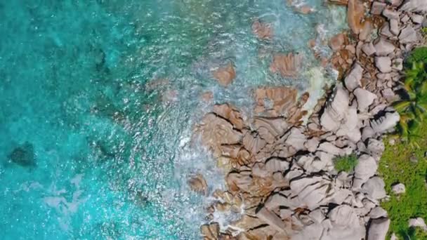 4k letecký pohled vertikální video vlny přijíždějící na skalnaté žulové skály ostrova La Digue. Křišťálově čistá voda s velkou viditelností — Stock video