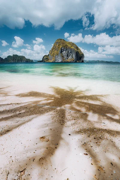 Palms shadows on tropical Las cabanas beach with unique amazing Pinagbuyutan island in background. Beautiful landscape scenery in El Nido, Palawan, Philippines