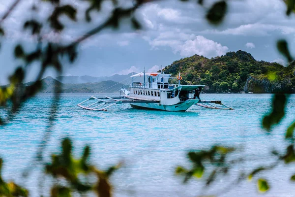 Pariwisata penyelam perahu di biru laguna cadlao dibingkai oleh daun. Pulau melompat tur, El Nido, Palawan, Filipina — Stok Foto
