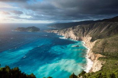 Kefalonya 'nın pitoresk pürüzlü kıyı şeridinde rüya gibi bir atmosfer. Overcast hava, derin bulutlar, fırtına deniz ve güneş ışığı, Cephalonia, Iyon Adaları, Yunanistan